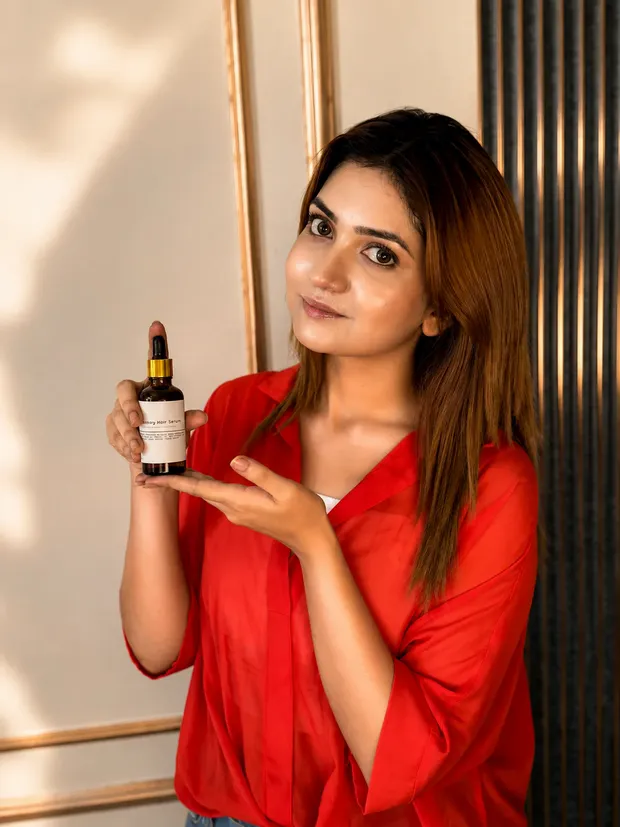 লাল শার্ট পরা তরুণী হাতের তালুতে The Formulate রোজমেরি হেয়ার সিরাম দেখাচ্ছেন